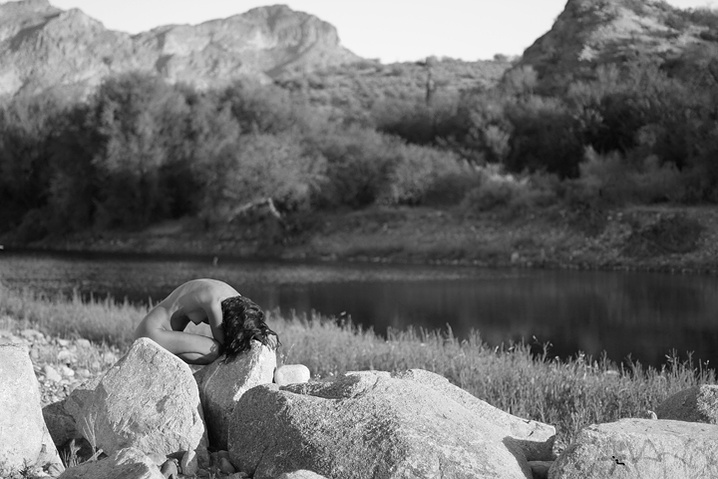 Between the Stones: Stillness becomes spectacle in this surreal lakeside where the body folds inward against the monumental calm of the surrounding landscape, with the distant mountains and reflective water creating a feeling of transcendence.